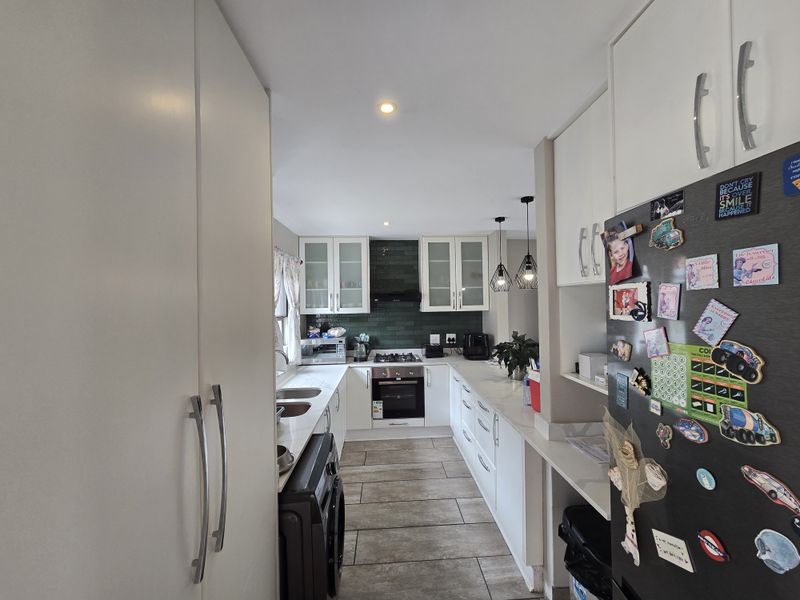 A well-maintained kitchen featuring white cabinetry, dark green tiled backsplash, gas hob, electric oven, and modern tiled flooring.