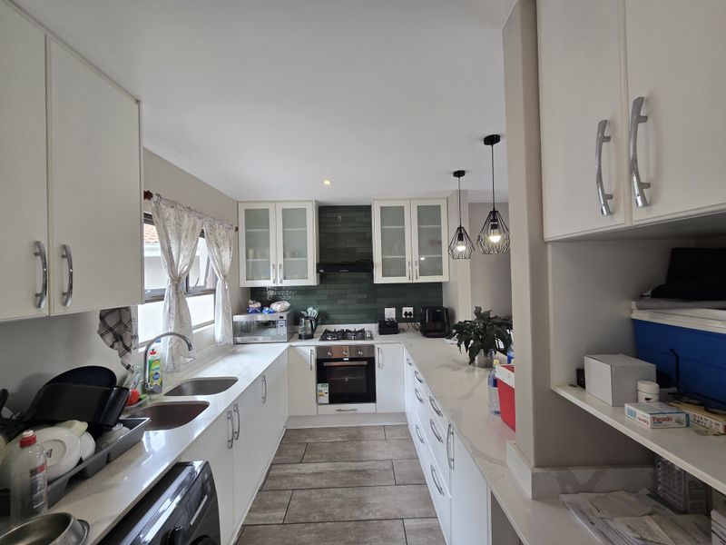Modern kitchen featuring white cabinetry, stone countertops, a gas hob with electric oven, and a stylish green tiled backsplash.