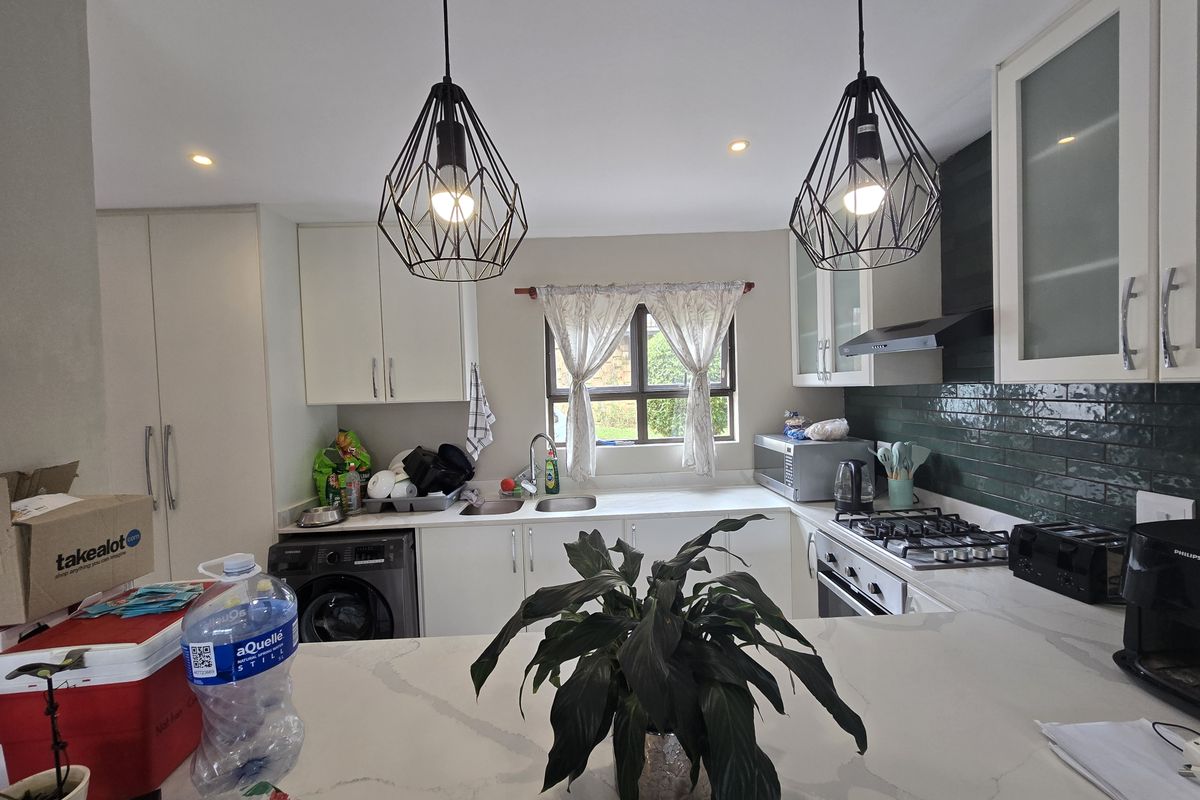 Modern kitchen featuring white cabinetry, stone countertops, a gas hob, integrated appliances, and stylish pendant lighting with a green subway tile backsplash.