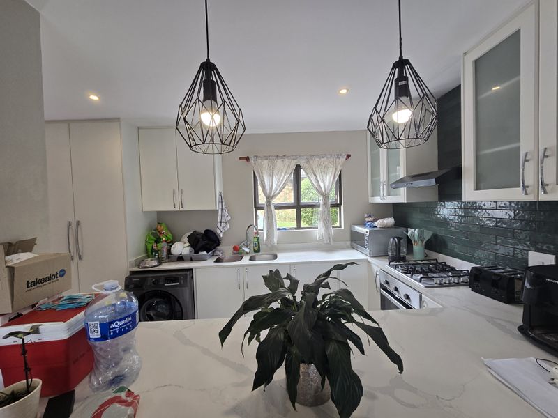 Modern kitchen featuring white cabinetry, stone countertops, a gas hob, integrated appliances, and stylish pendant lighting with a green subway tile backsplash.
