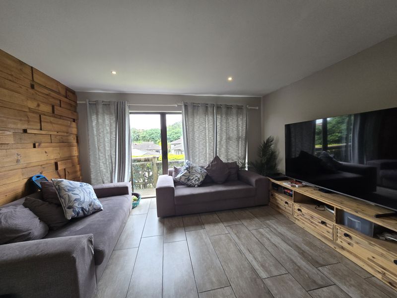 A comfortable living room featuring a timber accent wall, tiled flooring, and a sliding glass door providing access to the outdoor area.