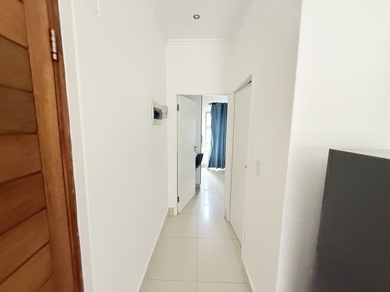 A clean, neutral hallway featuring tiled flooring and recessed ceiling lighting, providing access to adjacent rooms within the apartment.
