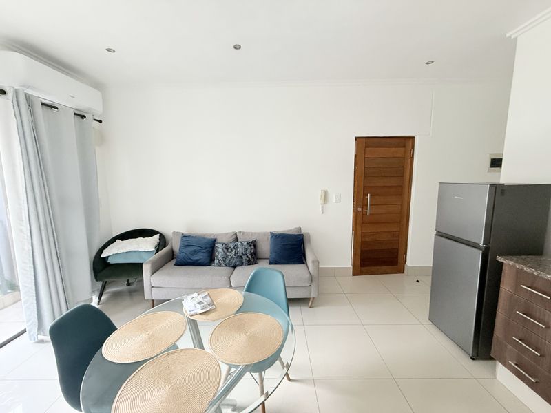 An open-plan living and dining area featuring tiled flooring, recessed lighting, an air conditioning unit, and direct access to a wooden door.