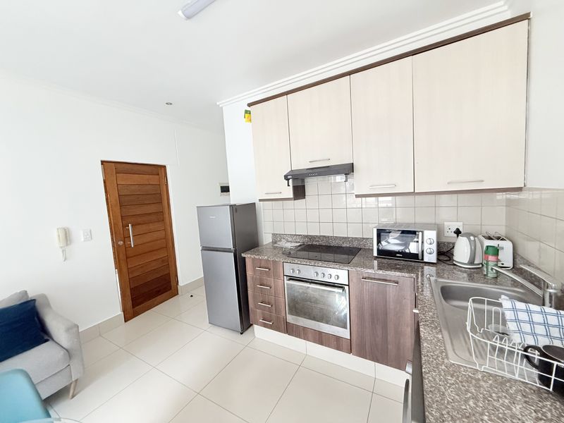 A functional kitchen featuring granite countertops, built-in cabinetry, a tiled backsplash, and integrated appliances including an oven and hob.