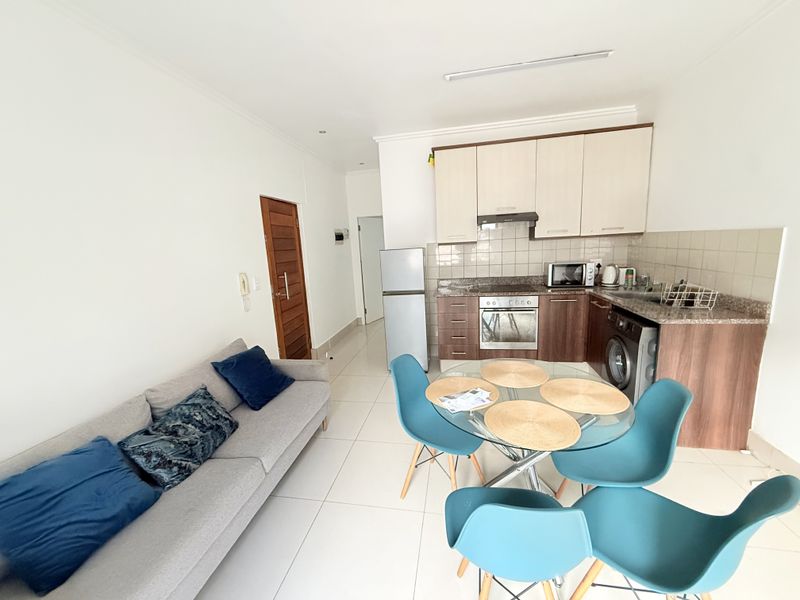 Open-plan living and kitchen area featuring tiled flooring, granite countertops, and built-in cabinetry with integrated appliances.