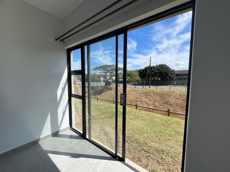 A bright, empty patio area featuring tiled flooring and large sliding glass doors that open onto a grassy outdoor space.