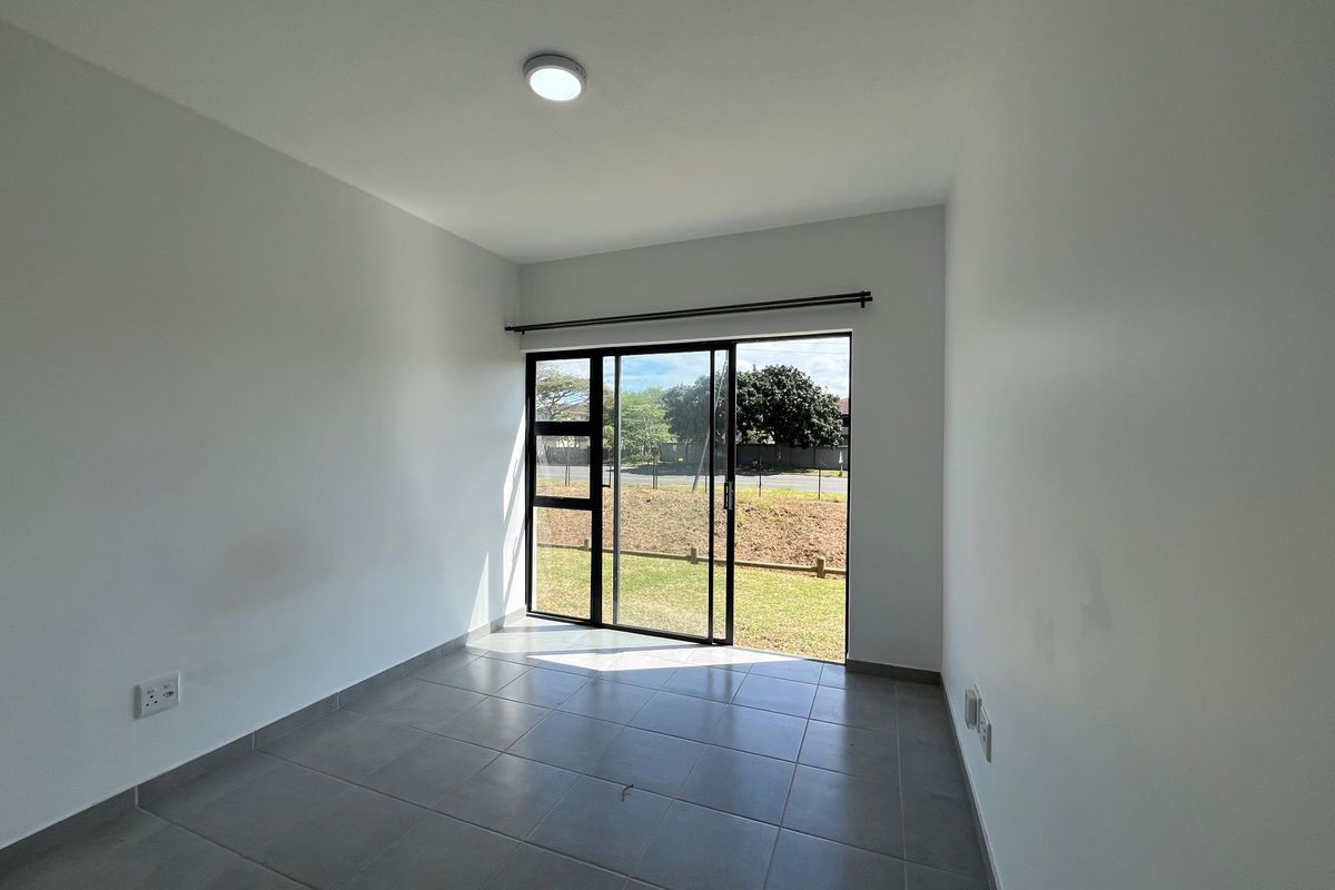 A bright, empty bedroom featuring neutral tiled flooring and a large sliding glass door providing direct access to the outdoor area.