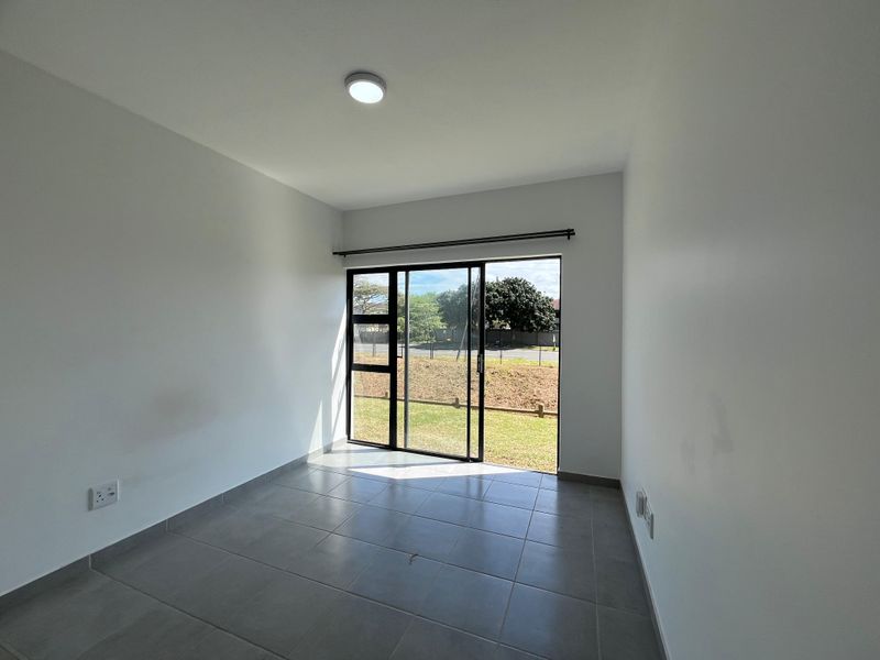 A bright, empty bedroom featuring neutral tiled flooring and a large sliding glass door providing direct access to the outdoor area.