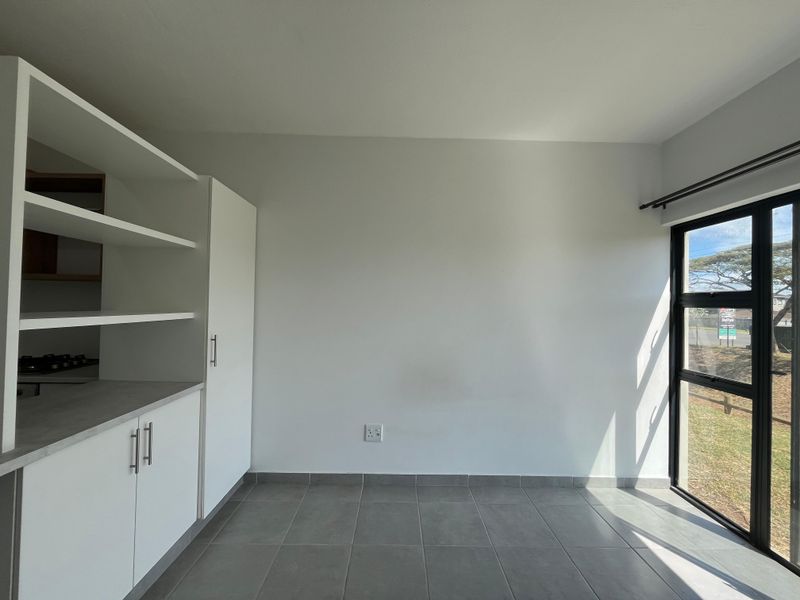 A bright, modern kitchen area featuring clean white cabinetry, tiled flooring, and large windows allowing for ample natural light.