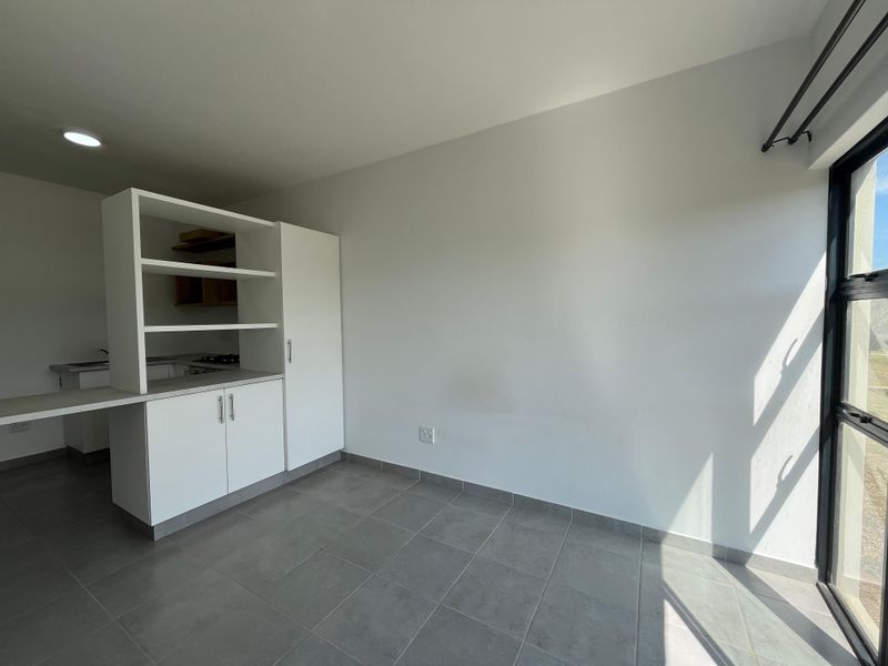 Bright open-plan living area featuring modern tiled flooring, built-in kitchen cabinetry, and large windows allowing for ample natural light.
