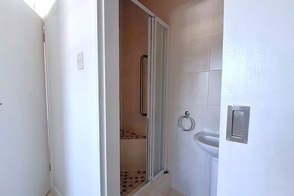A functional bathroom featuring a shower enclosure with a grab rail and a pedestal basin with tiled wall finishes.