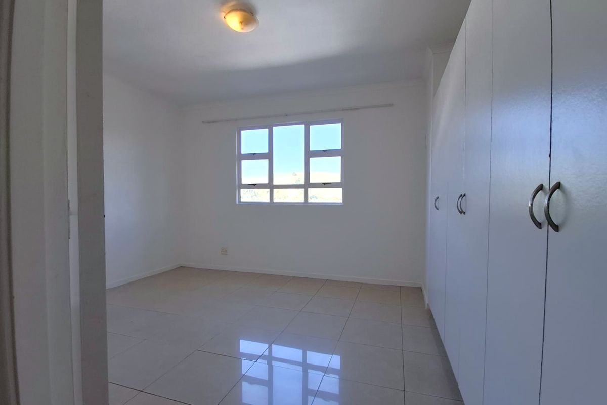 A bright, empty bedroom featuring neutral tiled flooring and extensive built-in cupboard storage, offering a clean and versatile space.