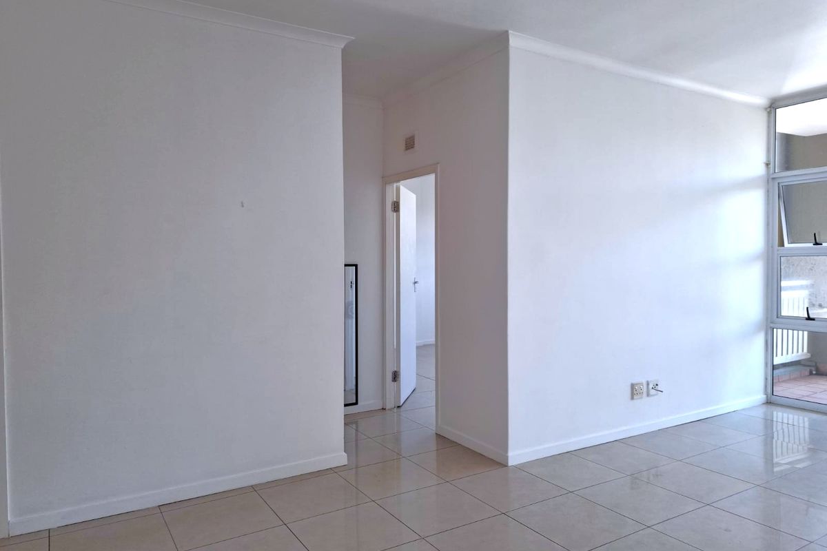 A bright, empty living area featuring neutral tiled flooring, coved ceilings, and large aluminium-framed windows allowing for natural light.