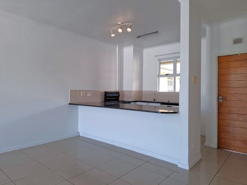 An open-plan living and kitchen area featuring tiled flooring, a granite breakfast bar, and a functional kitchen layout with built-in appliances.