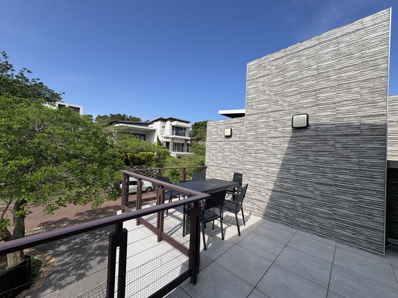 A spacious outdoor balcony featuring modern stone-clad walls, tiled flooring, and secure railings, offering a pleasant elevated view of the surrounding neighborhood.