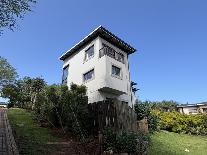 A multi-story townhouse exterior featuring a private balcony, modern architectural lines, and established garden surroundings.