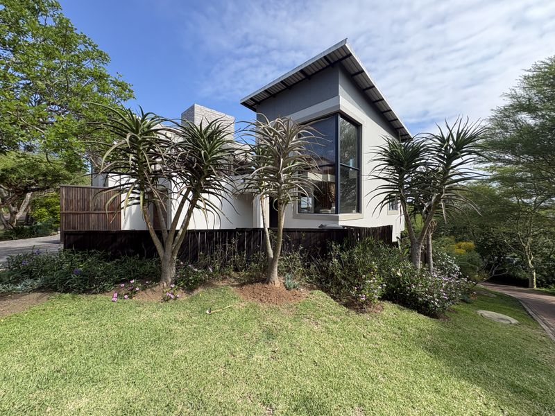A modern townhouse exterior featuring a pitched roof, large feature window, and well-maintained landscaped garden with mature trees.