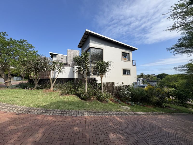 A modern multi-level townhouse featuring a paved driveway, landscaped garden, and contemporary architectural design with stone accents and a balcony.