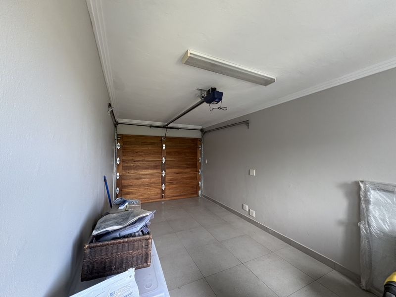 A clean, well-maintained garage featuring tiled flooring, a wooden sectional door, and an automated garage door motor.