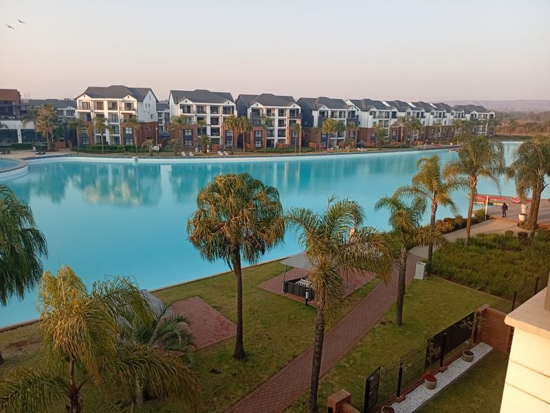 A scenic view of a large communal swimming pool surrounded by landscaped gardens and modern apartment buildings within a residential estate.