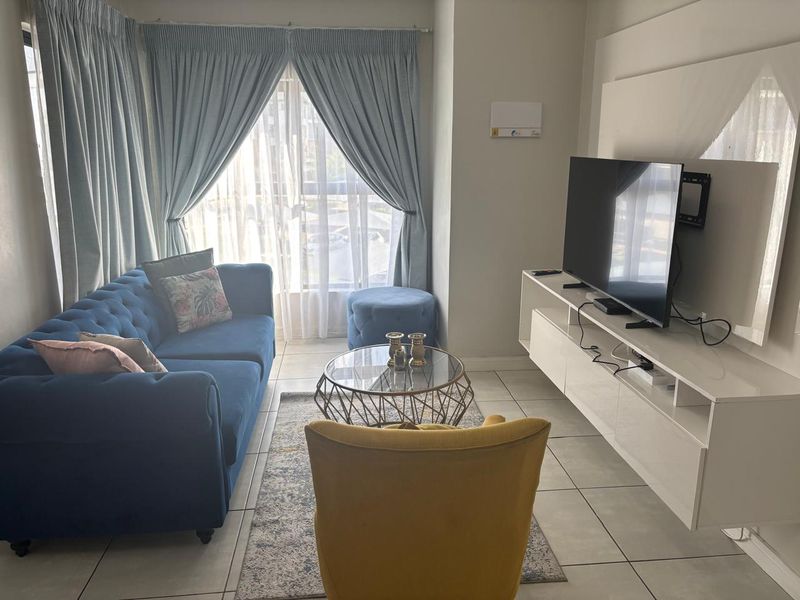 A well-lit living room featuring tiled flooring and large windows with curtains, providing a comfortable and functional space.