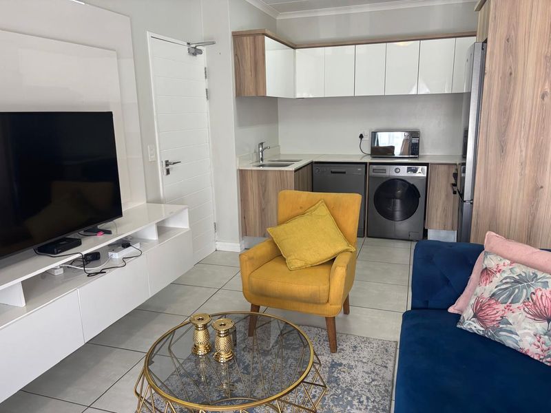Modern open-plan living area featuring a compact kitchen with built-in cabinetry, integrated appliances, and sleek tiled flooring throughout.