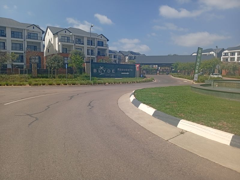 Street view approach to The Blyde residential estate, featuring landscaped grounds, paved roads, and modern apartment building architecture.