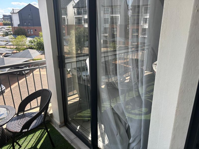 A private balcony featuring a metal balustrade and sliding glass door access, overlooking the apartment complex grounds.