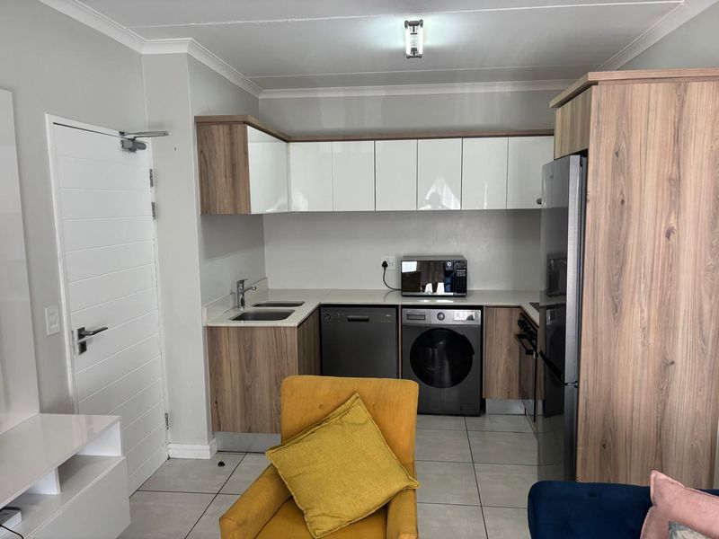 A compact, modern kitchen featuring wood-grain and white cabinetry, tiled flooring, and integrated appliance spaces, offering a clean and functional layout.