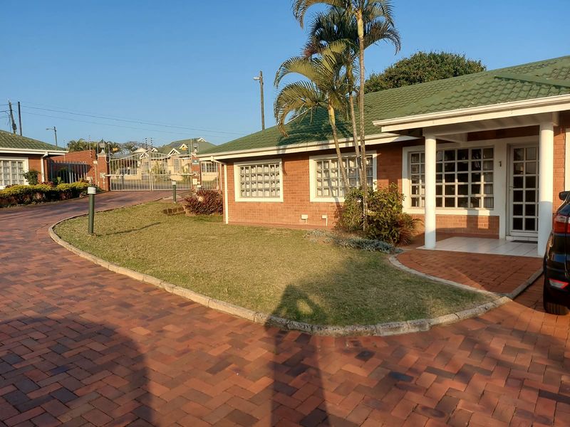 Front exterior view of a brick apartment unit featuring a paved driveway, covered entrance porch, and established garden area.