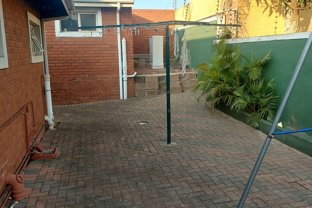 A paved rear courtyard area featuring brick boundary walls with electric fencing and a rotary clothesline, offering a functional outdoor utility space.