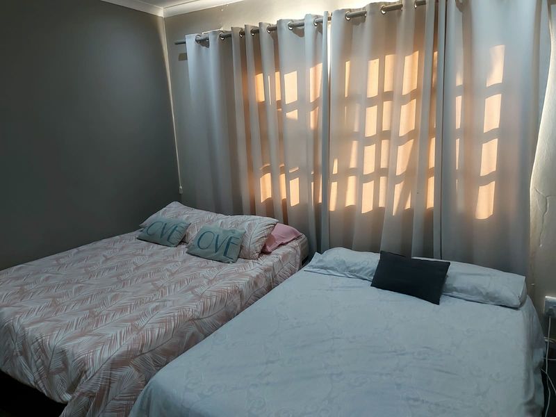 A bedroom featuring neutral wall tones and floor-to-ceiling curtains, providing a functional space with natural light filtering through.