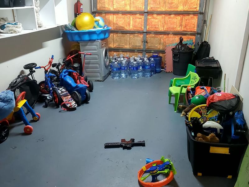 A functional garage space featuring a sectional door, built-in wall shelving, and painted concrete flooring, currently utilized for storage.