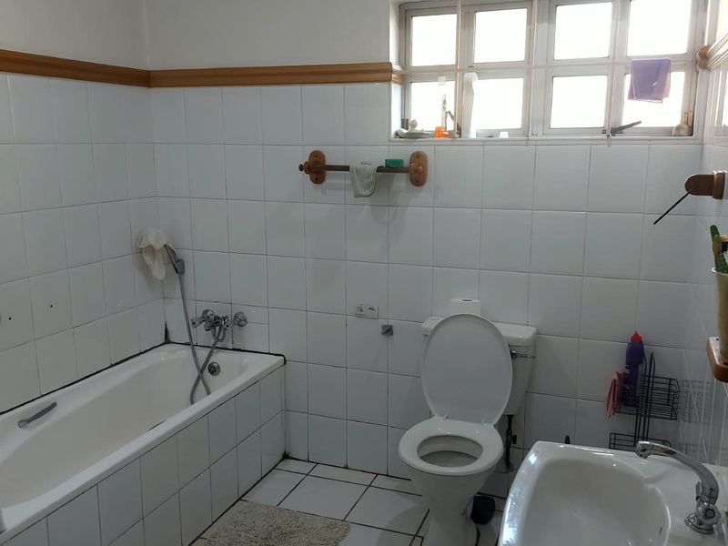 A functional bathroom featuring a built-in bathtub, pedestal sink, and toilet with white wall and floor tiling throughout.