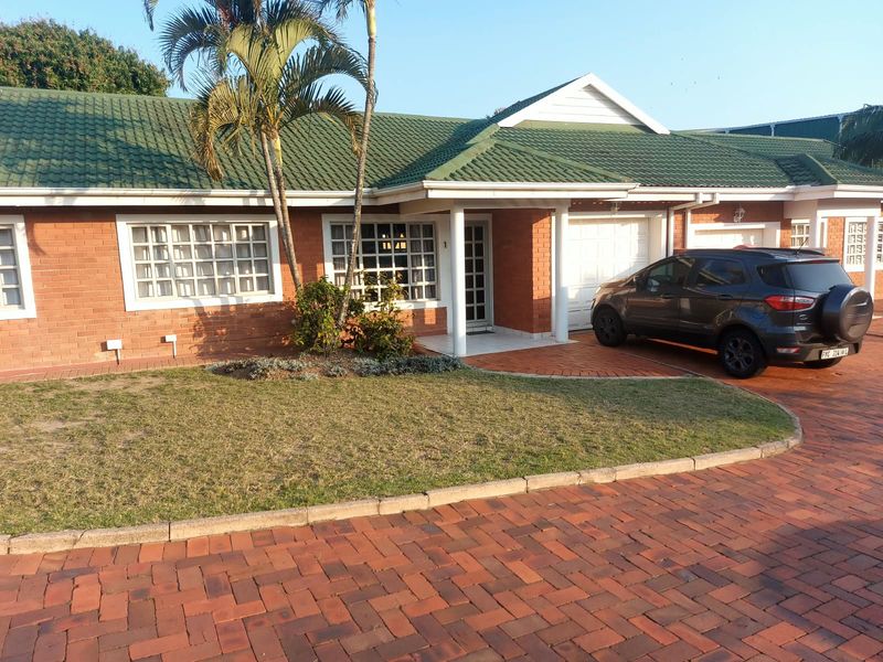 Front elevation of a single-story brick apartment featuring a green tiled roof, paved driveway, and a private garage entrance.