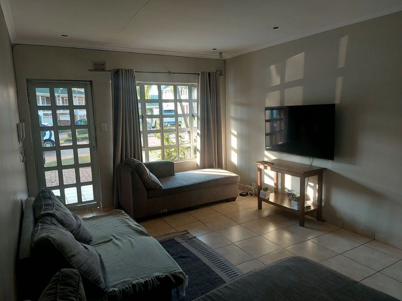 A comfortable living room featuring tiled flooring, recessed lighting, and a large window with natural light, providing a functional and inviting space.