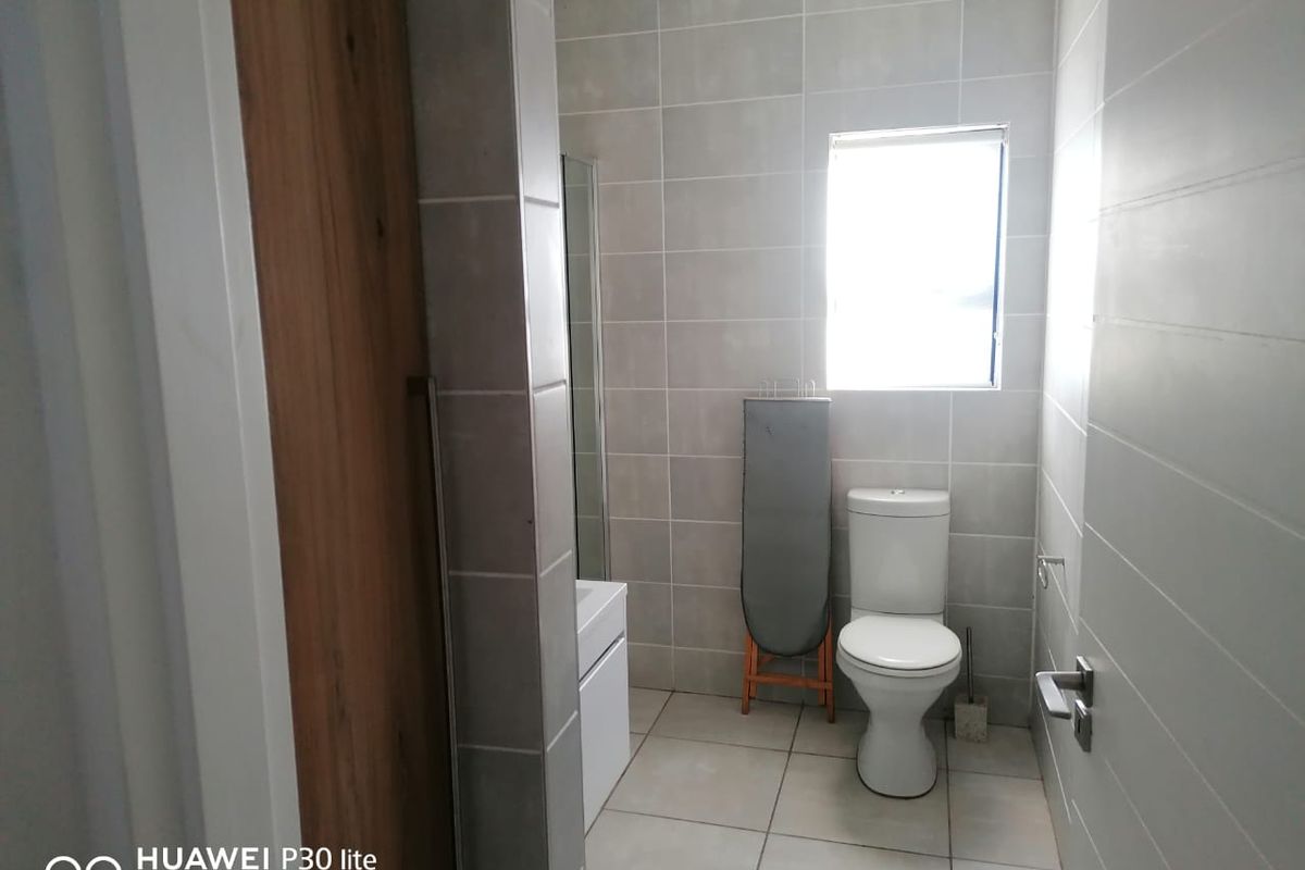 A modern bathroom featuring neutral wall and floor tiles, a white toilet, and a vanity cabinet with a shower enclosure.
