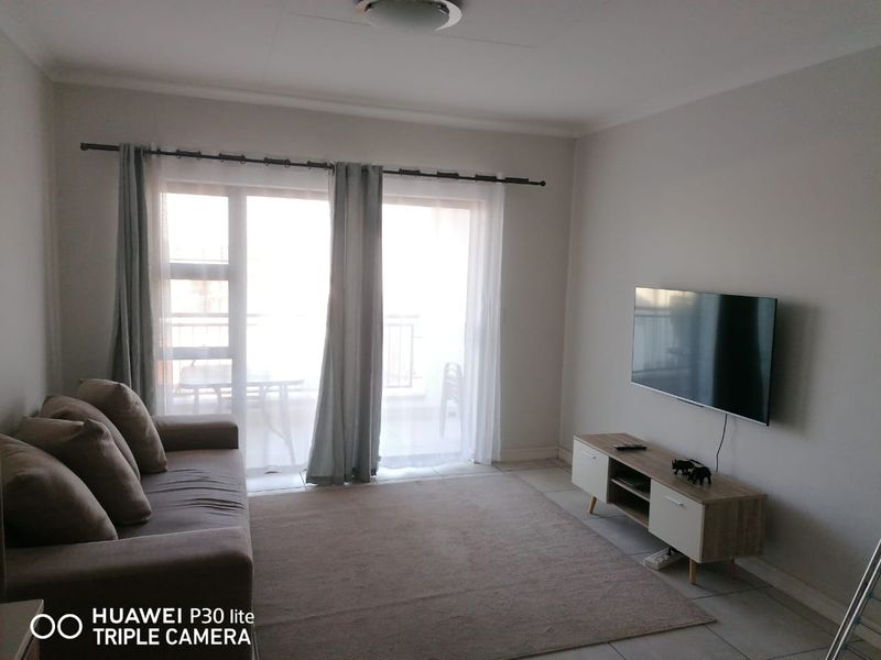 A bright living room featuring tiled flooring and a large sliding glass door providing access to an outdoor balcony area.