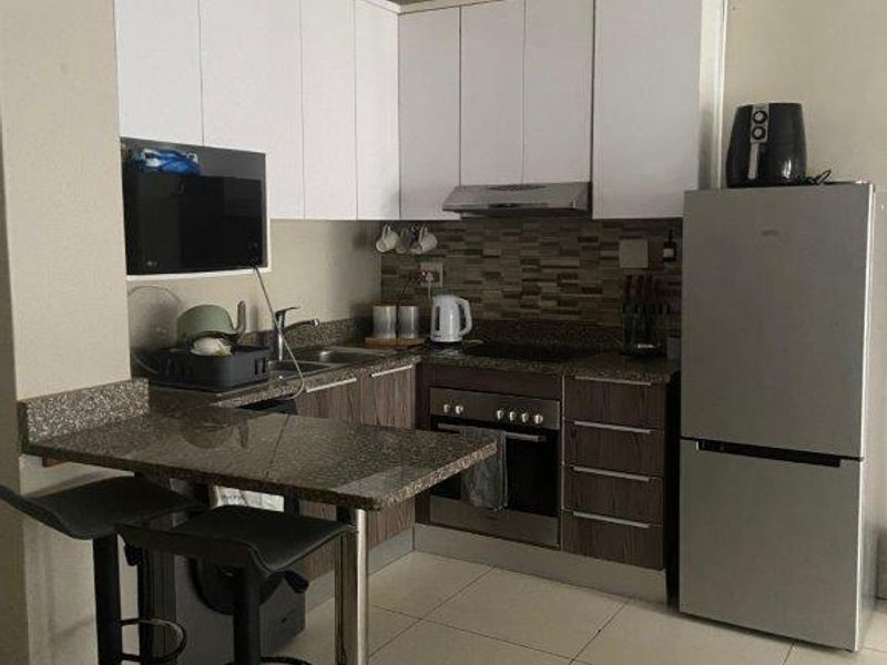 Compact kitchen featuring granite countertops, built-in cabinetry, stainless steel oven and hob, and tiled flooring.
