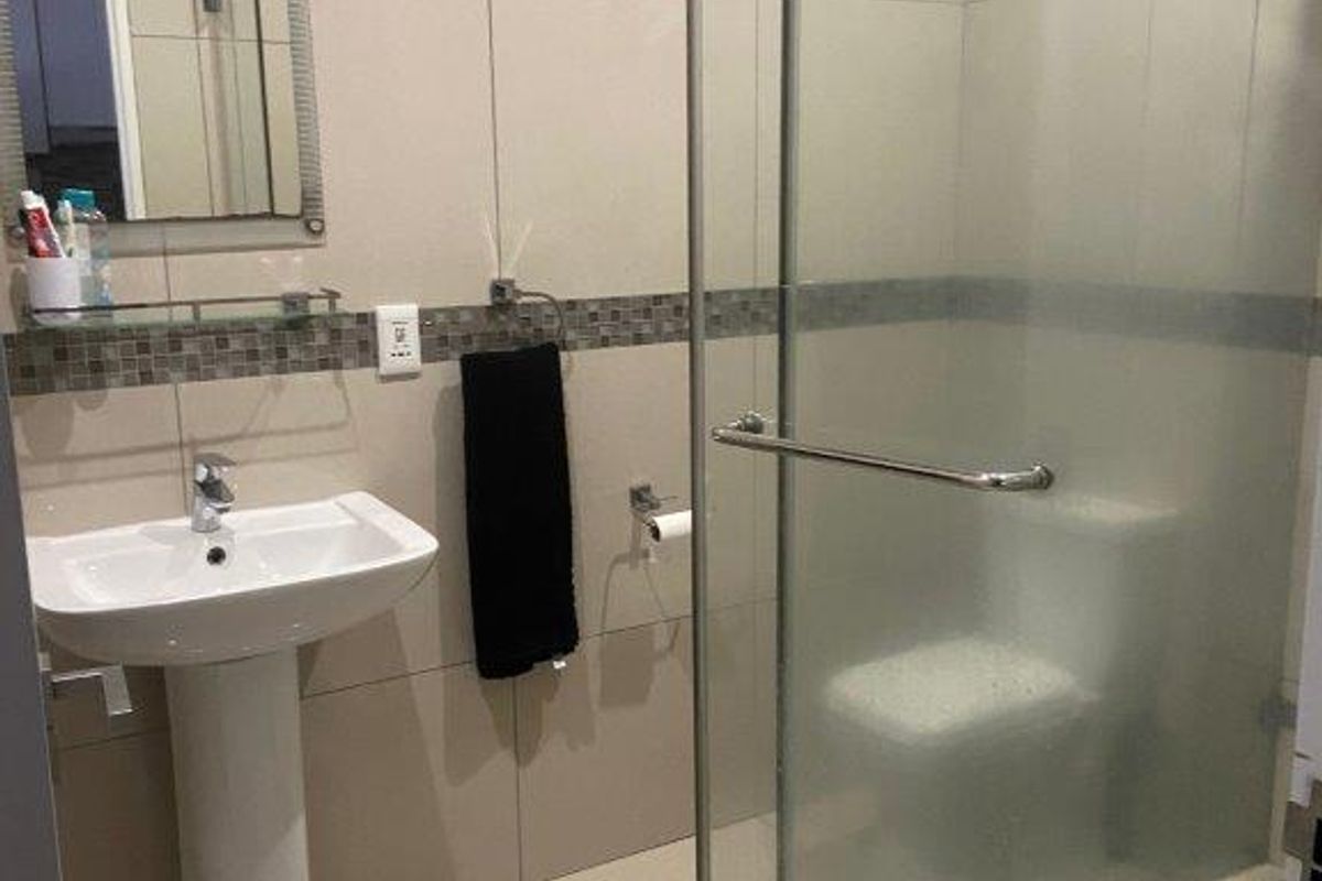 A functional bathroom featuring a pedestal basin, tiled walls, and a glass-enclosed shower area with modern fixtures.