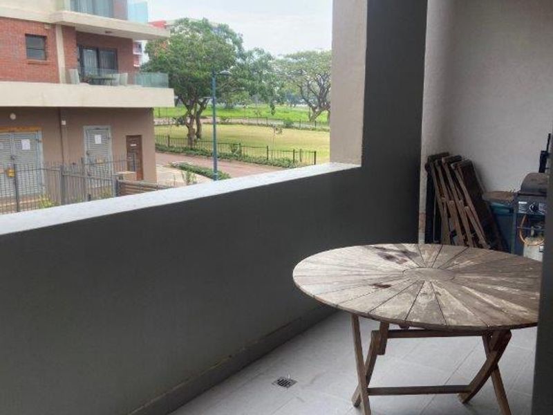 A covered balcony featuring tiled flooring, a ceiling light, and a solid balustrade, offering an open view of the surrounding complex grounds.