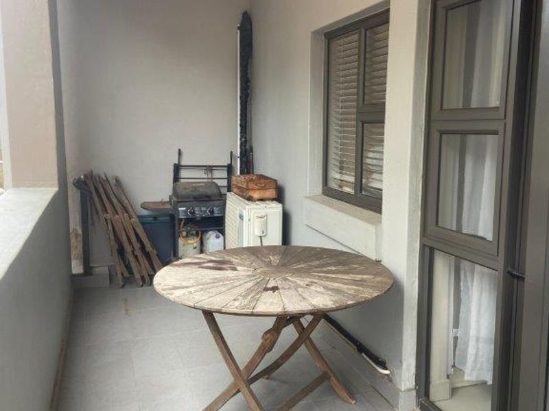A covered balcony featuring tiled flooring, a sliding glass door, and a window with blinds, providing a functional outdoor space.