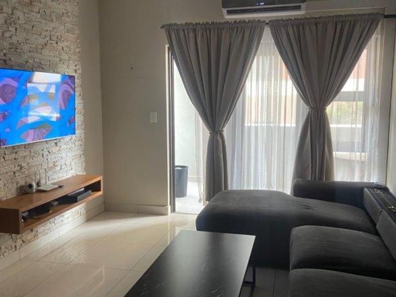 A modern living room featuring a textured stone accent wall, floating media console, tiled flooring, and direct access to a balcony through sliding glass doors.