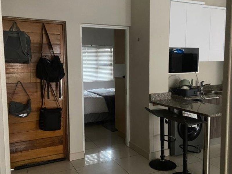 Open plan living area featuring a compact kitchen with granite countertops and tiled flooring, with direct access to an adjacent bedroom.