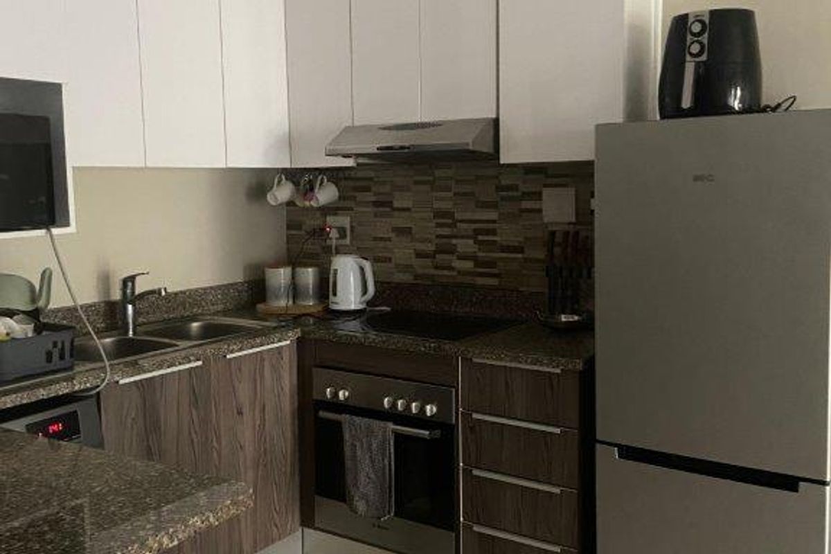 Modern kitchen featuring white upper cabinets, wood-grain lower cabinetry, stone countertops, mosaic tile backsplash, and integrated stainless steel appliances.