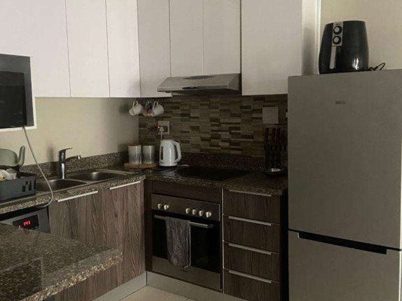 Modern kitchen featuring white upper cabinets, wood-grain lower cabinetry, stone countertops, mosaic tile backsplash, and integrated stainless steel appliances.