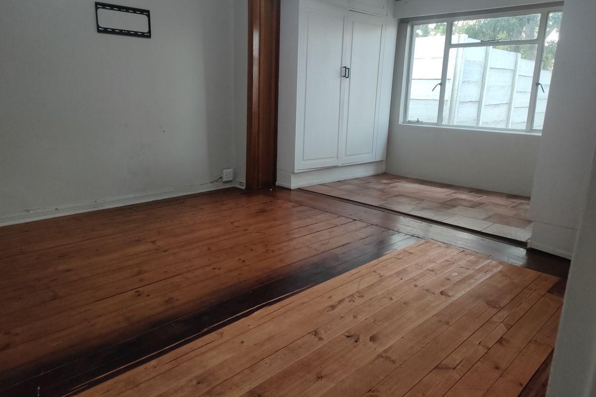 An empty bedroom featuring polished timber flooring, a tiled transition area, and built-in storage cupboards.