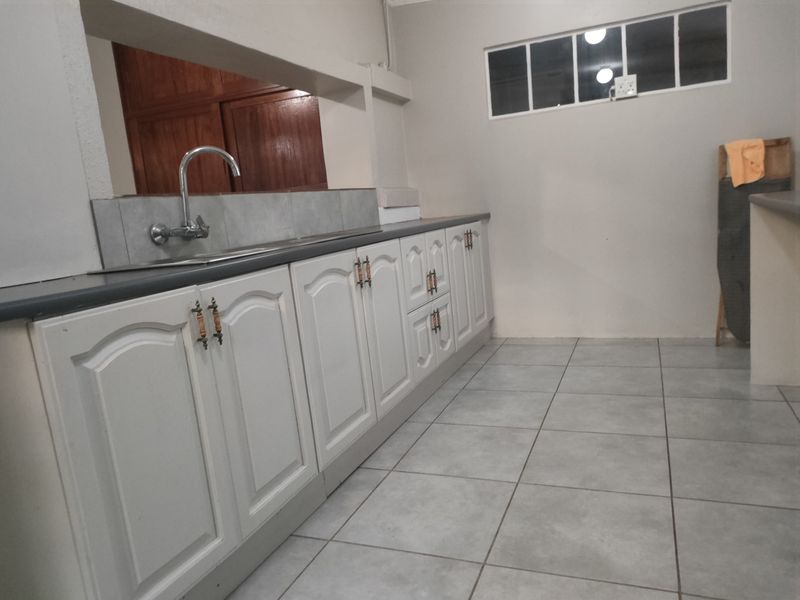 A functional kitchen area featuring white built-in cabinetry, a stainless steel sink, tiled splashbacks, and neutral floor tiles.