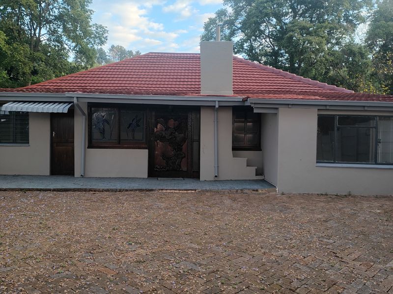 Front elevation of a single-story house featuring a tiled roof, chimney stack, and a paved driveway area.