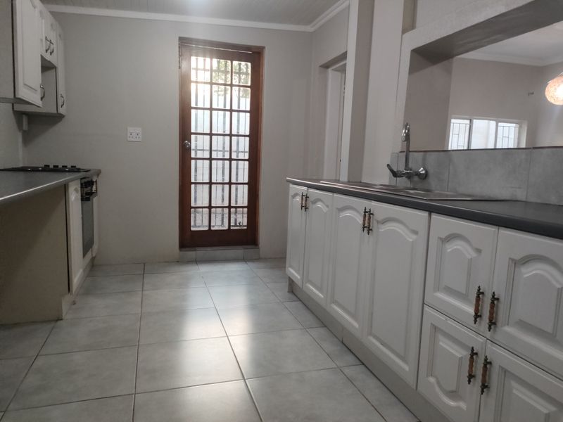A functional kitchen featuring white cabinetry, laminate countertops, built-in oven and hob, tiled flooring, and a timber-framed glass door leading to the exterior.